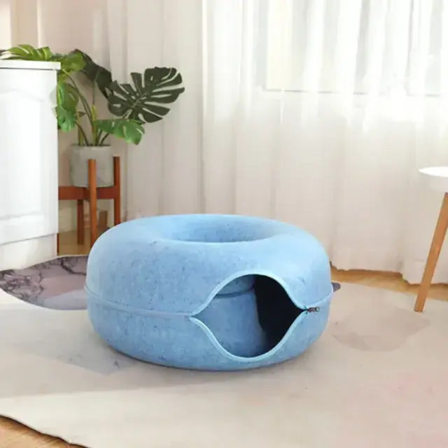 TAILTRAIL donut cat bed in blue felt material, featuring a cozy tunnel for cats, set in a bright interior.