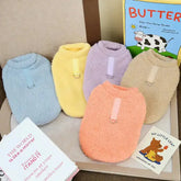 Plush Winter coats for dogs in pastel colors by TAILTRAIL, displayed with books on a soft surface